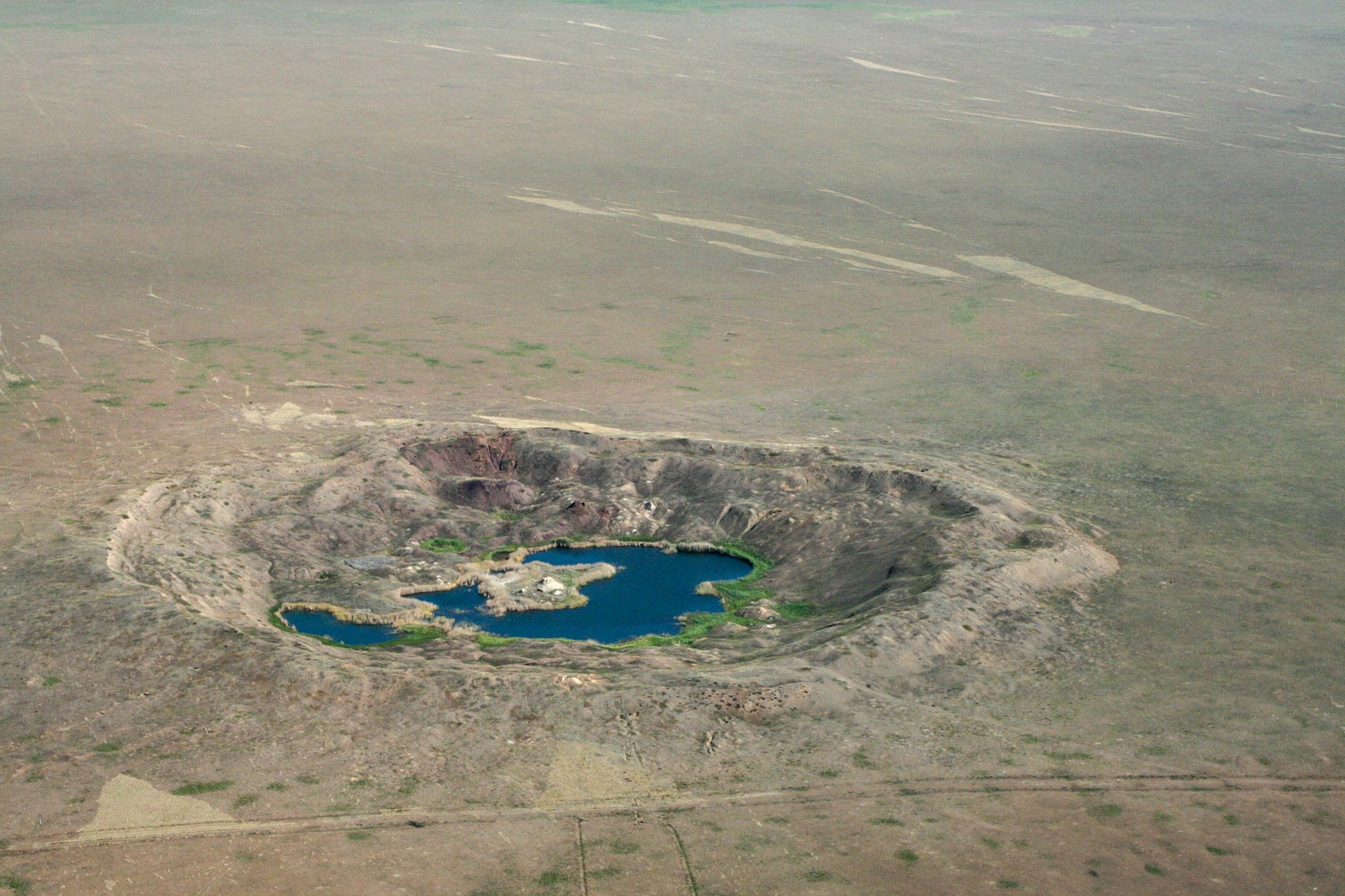 A crater in the ground filled with a murky substance and surrounded by barren land.