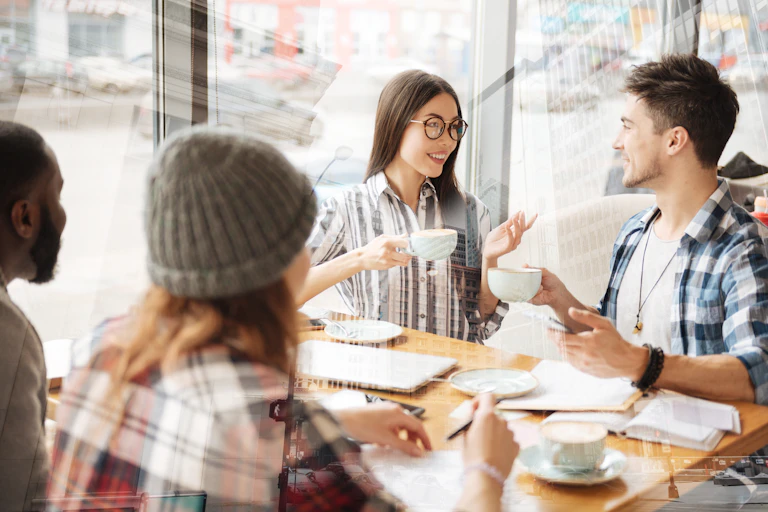 four diverse young people sit at a table at a cafe and talk