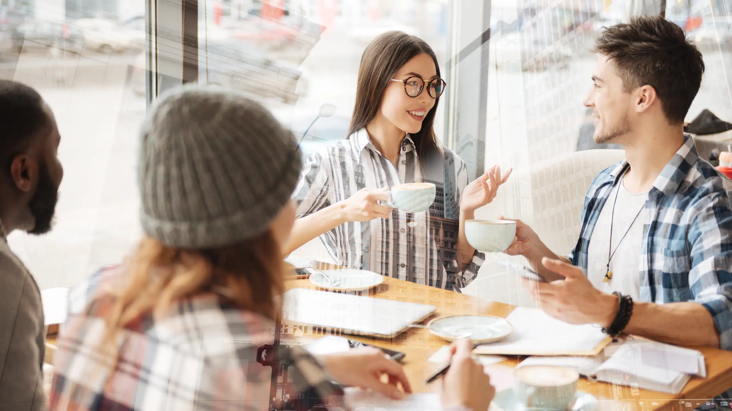 four diverse young people sit at a table at a cafe and talk