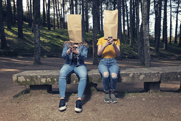Two people are on their phones with bags over their heads.