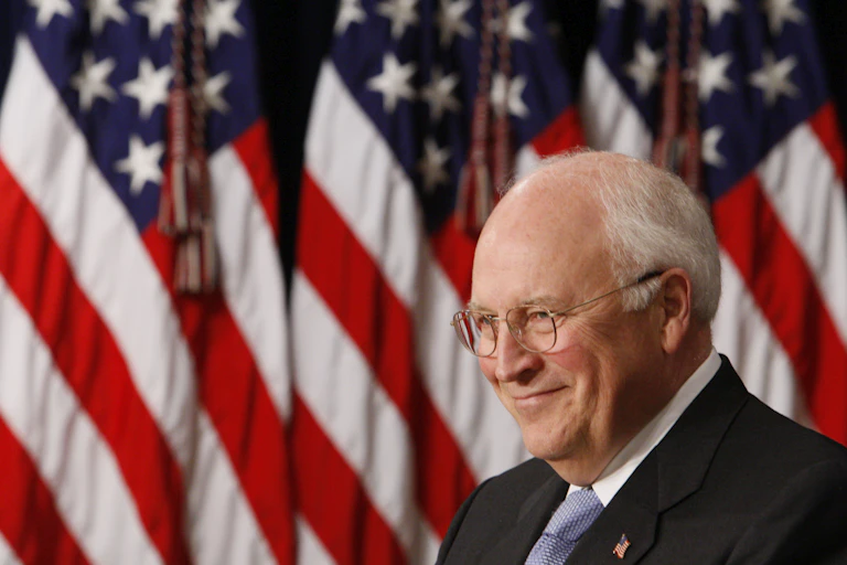 A man smiles, with American flags in the background.