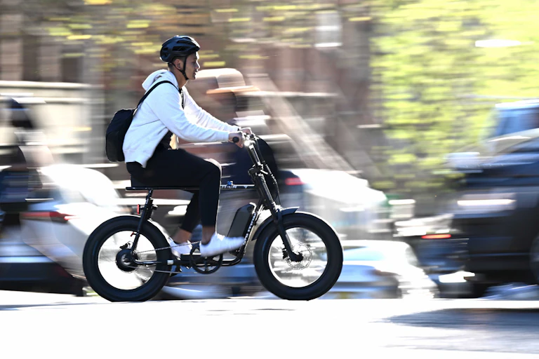 A young man rides an e-bike through traffic in Sydney.