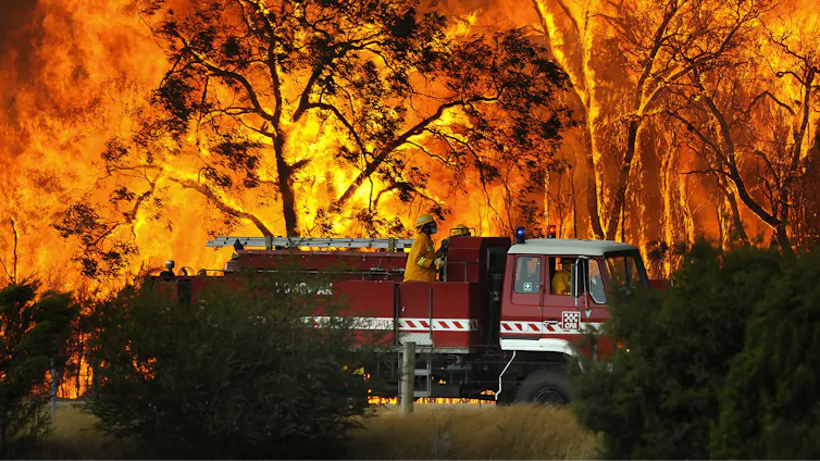 A fire truck in front of a raging forest fire.