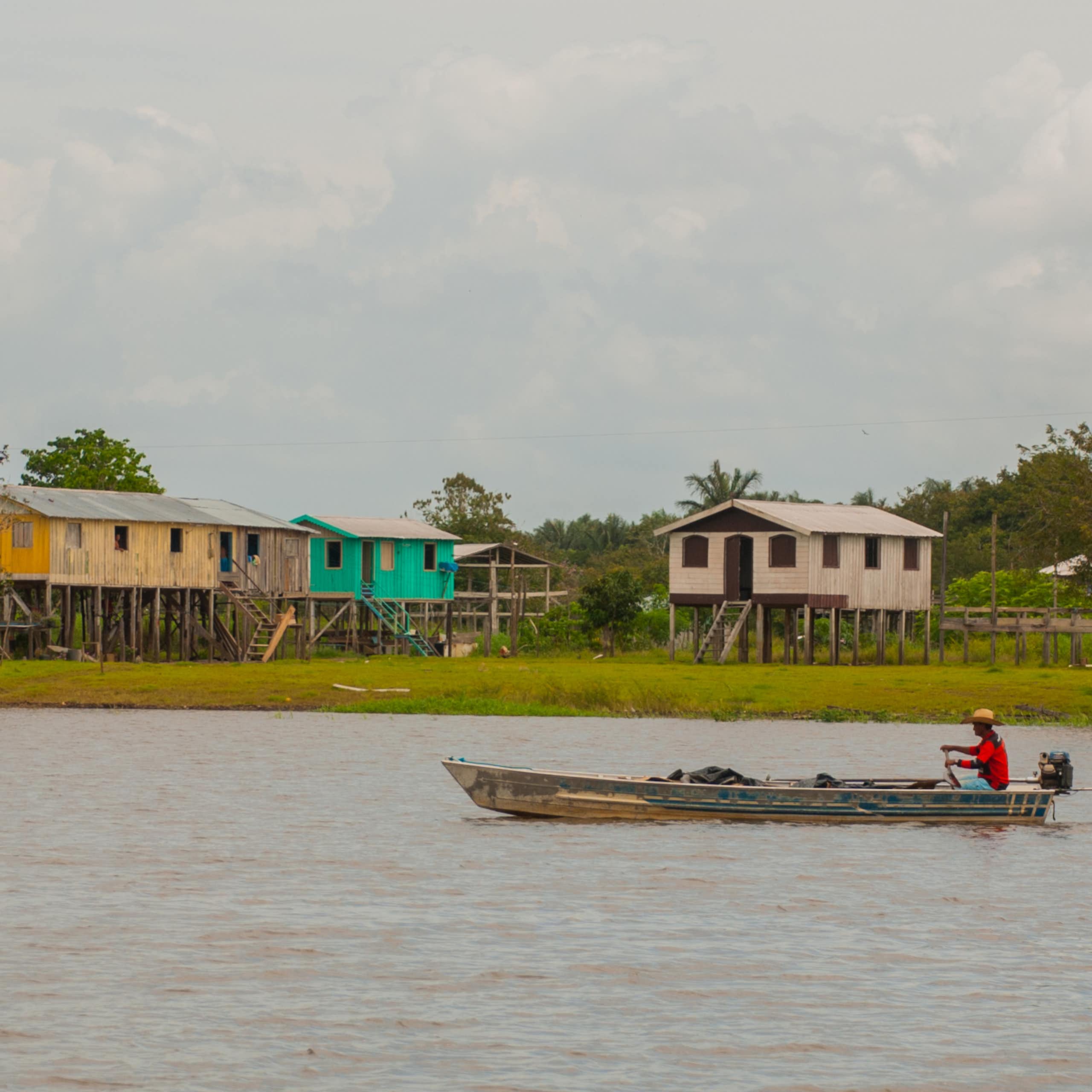 Una barca circula por un río con casas de colores en la orilla al fondo