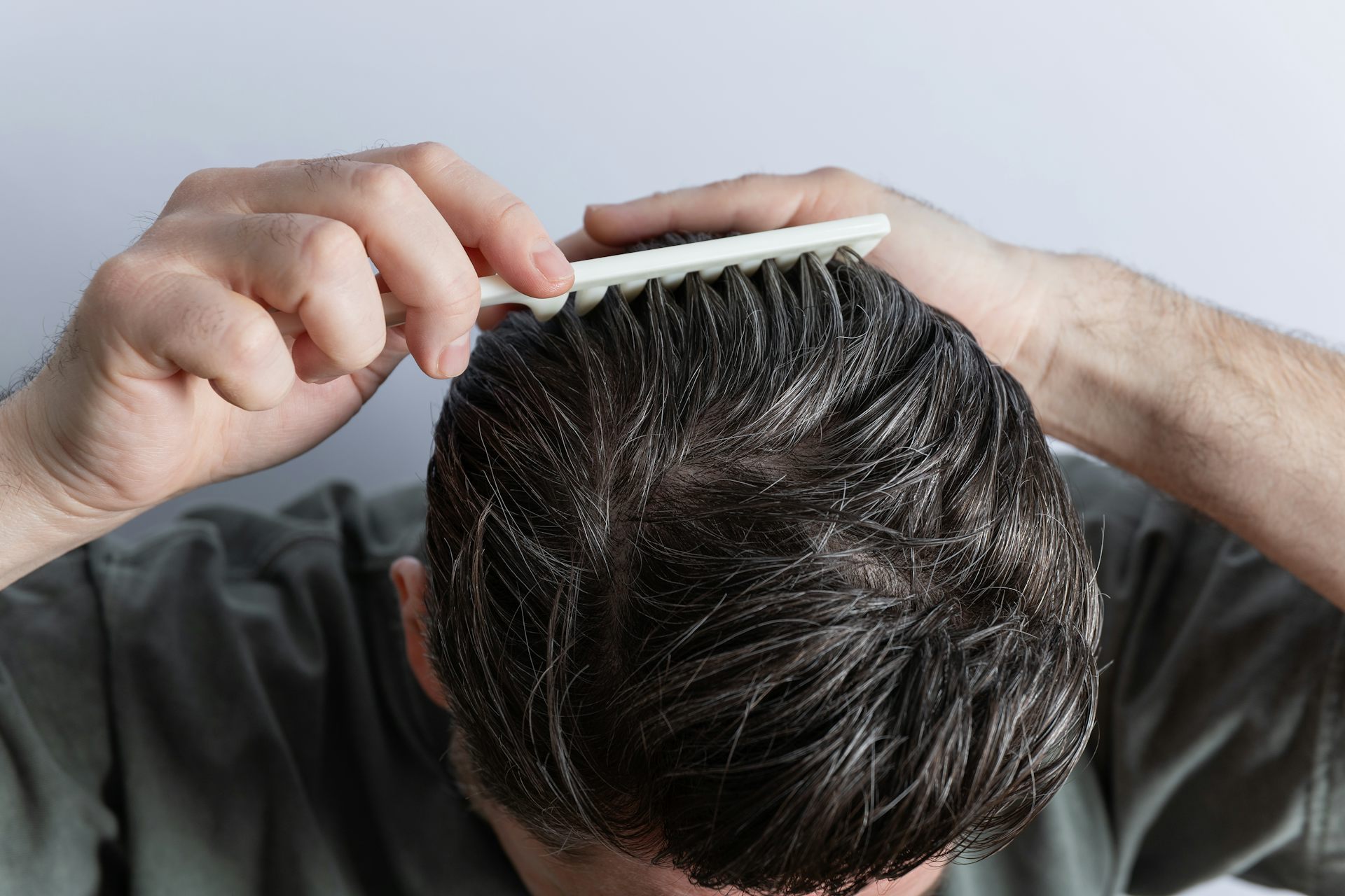 A man pushes a comb through his dark hair, which has some strands of grey throughout.