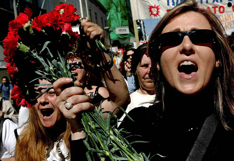 protesters on the streets of athens with a woman in the foreground holding a bunch of roses and chanting