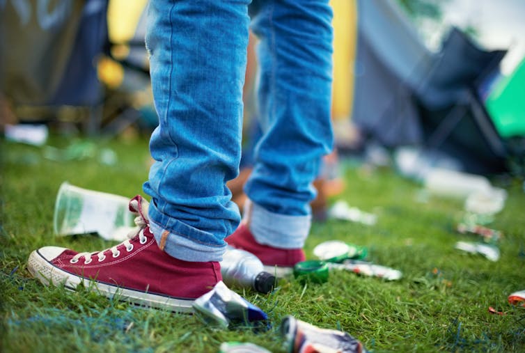 Person stood on grass surrounded by littered bottles and cans