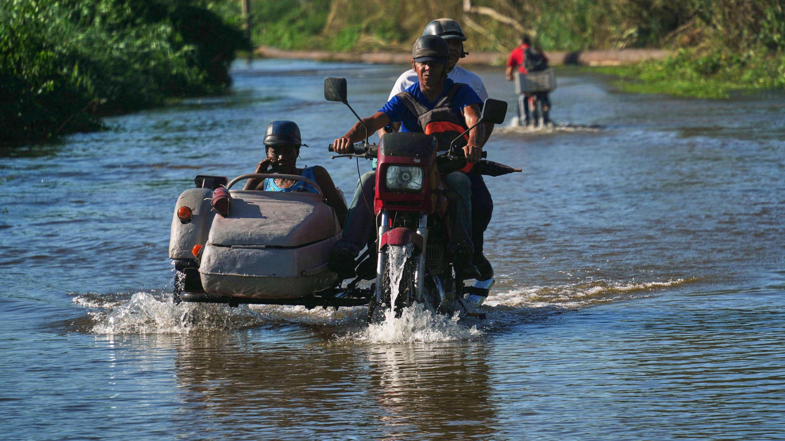 Cubans on a motorbike ride through a flooded road