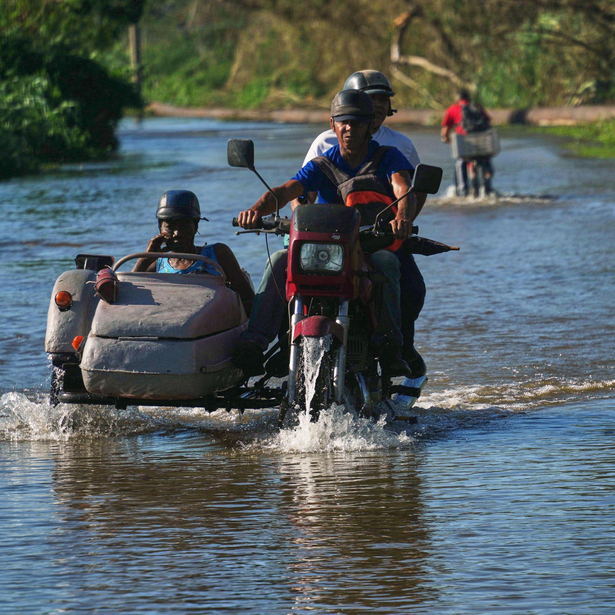 Cubans on a motorbike ride through a flooded road