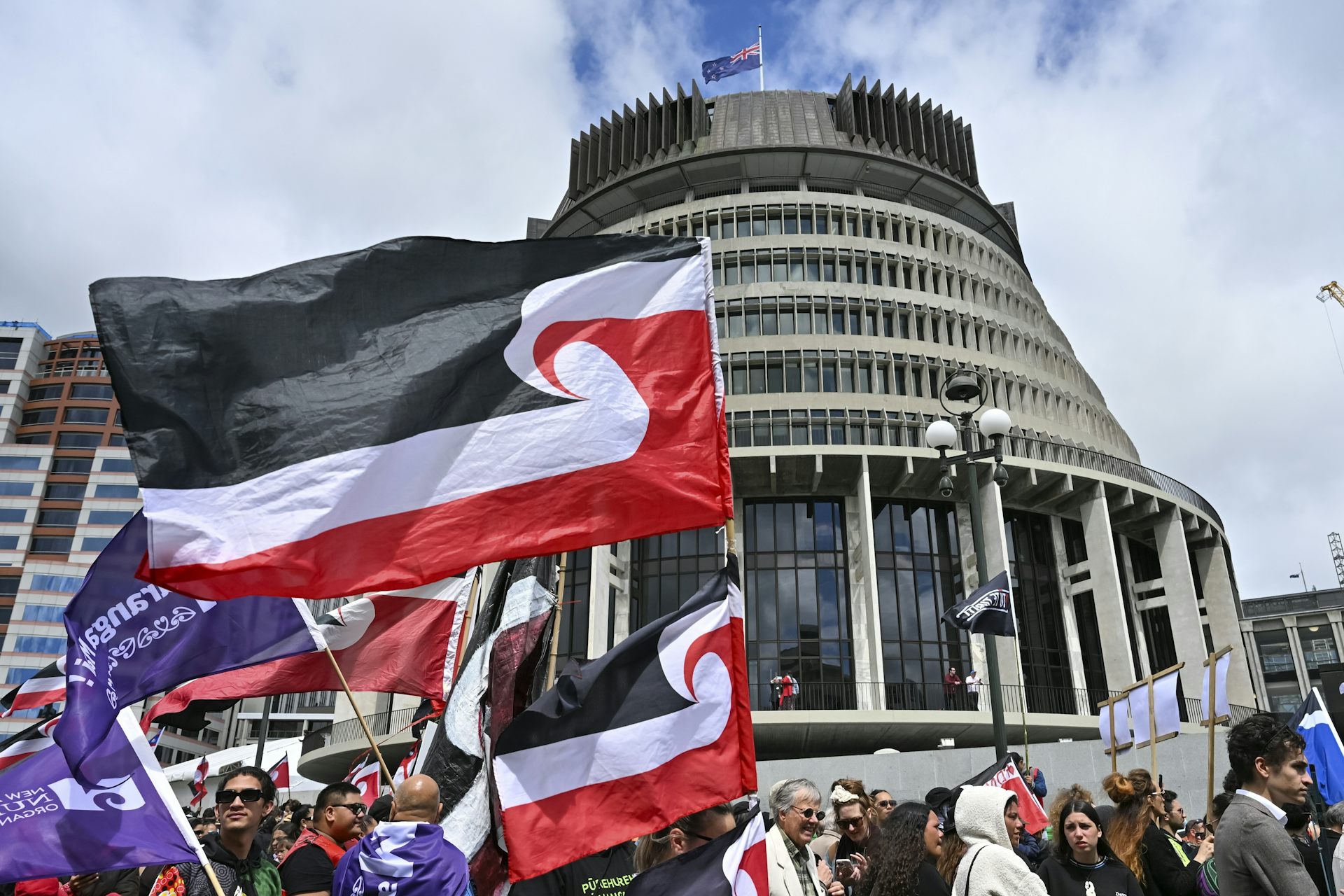 Protesters wave large red, white and black flags in front of a conical shaped building.