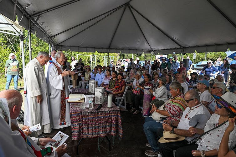 What does ‘pro-life’ imply? There’s no person resolution – even for advocacy teams that oppose abortion 1 A few priests in white robes stand behind a table in an outdoor tent full of seated people.