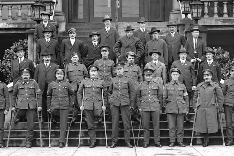 Men in overcoats in rows on steps, holding single crutches, many with an amputated leg.