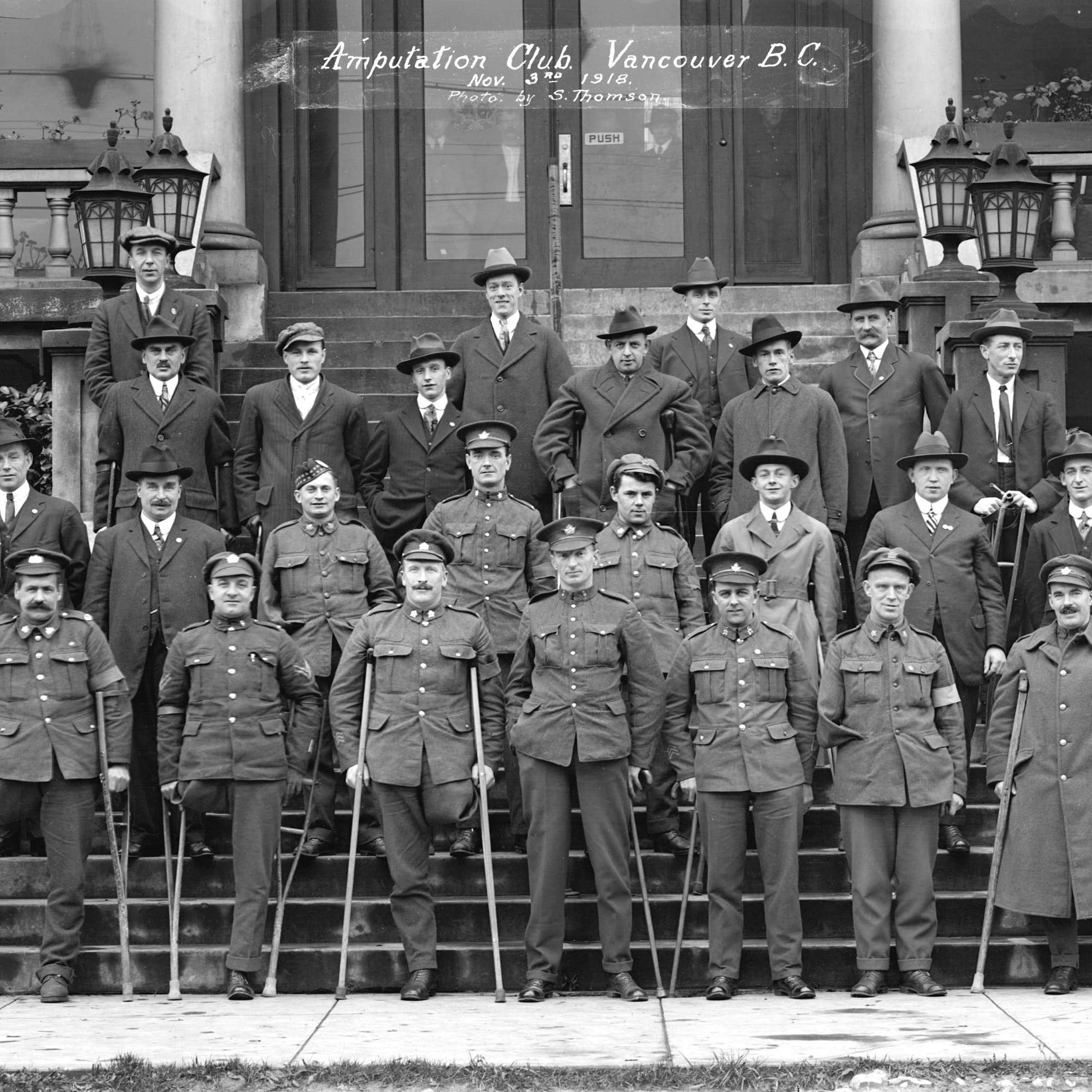 Men in overcoats in rows on steps, holding single crutches, many with an amputated leg.
