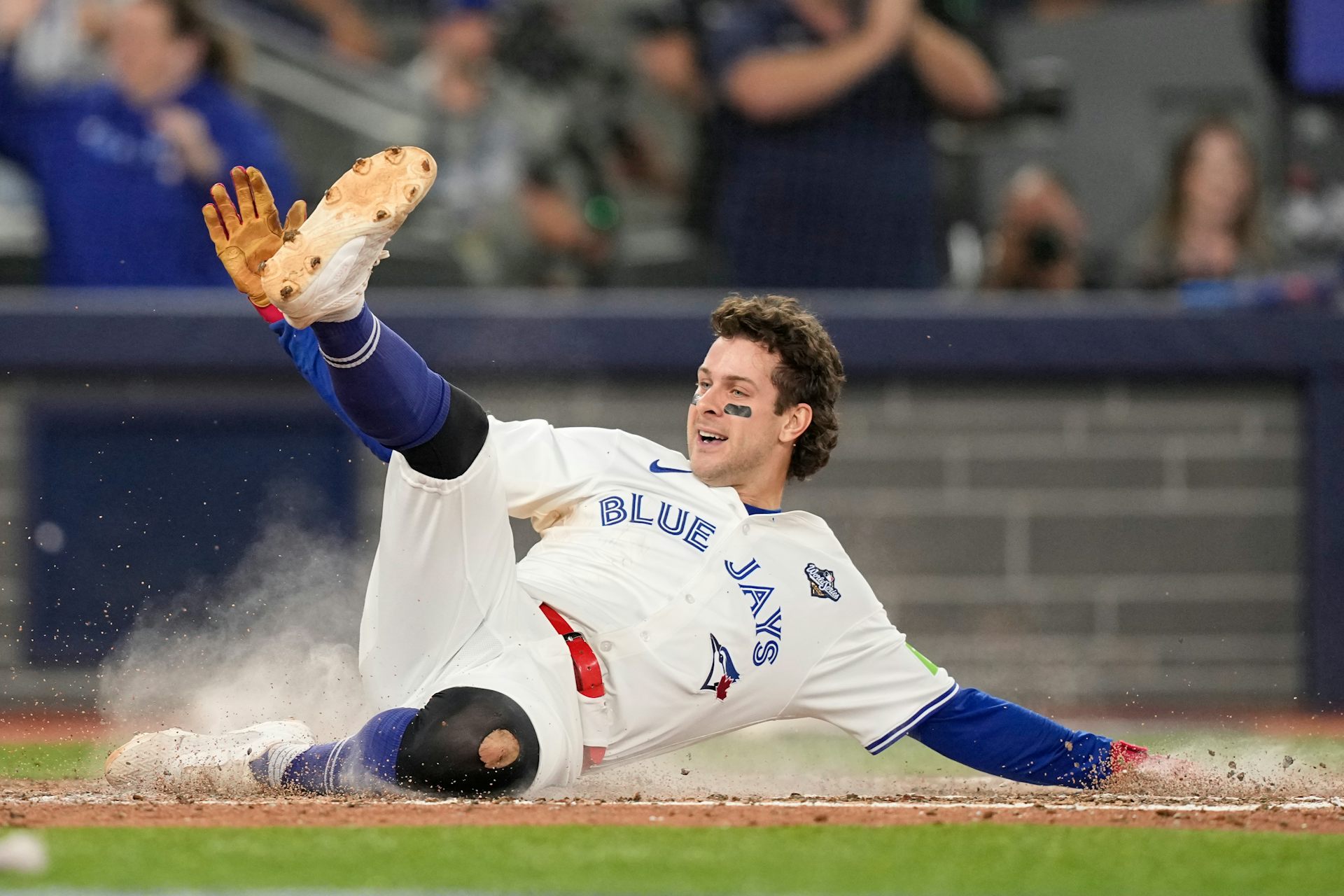 A baseball player slides across home plate with his leg up in the air and a smile on his.