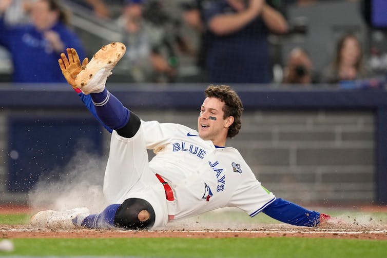 A baseball player slides across home plate with his leg up in the air and a smile on his.