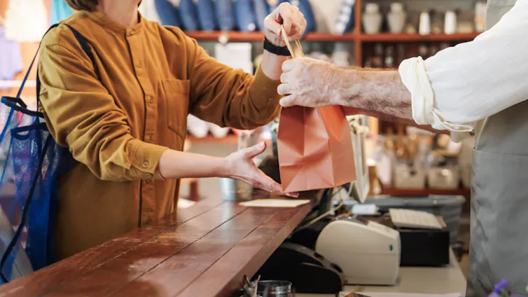 shopkeeper handing customer a shopping bag.