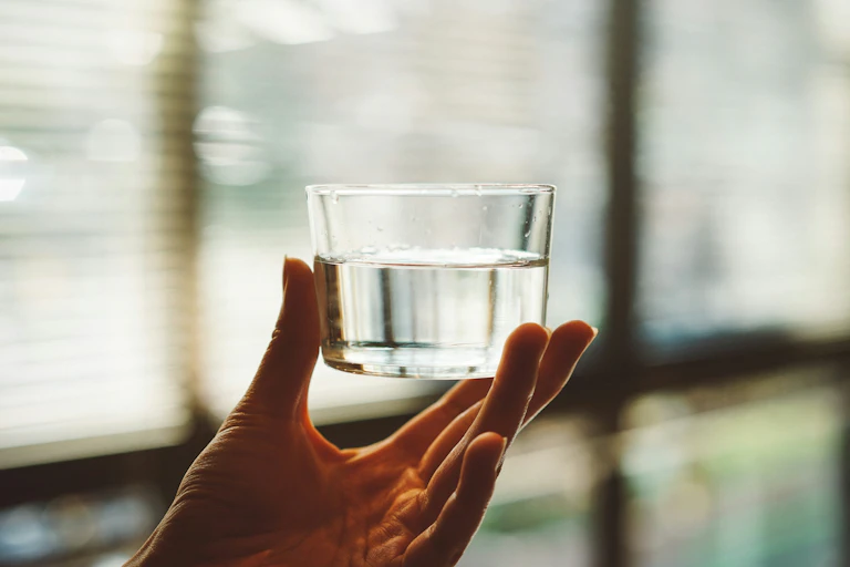A hand holding a small cup of clear water in sunlight.