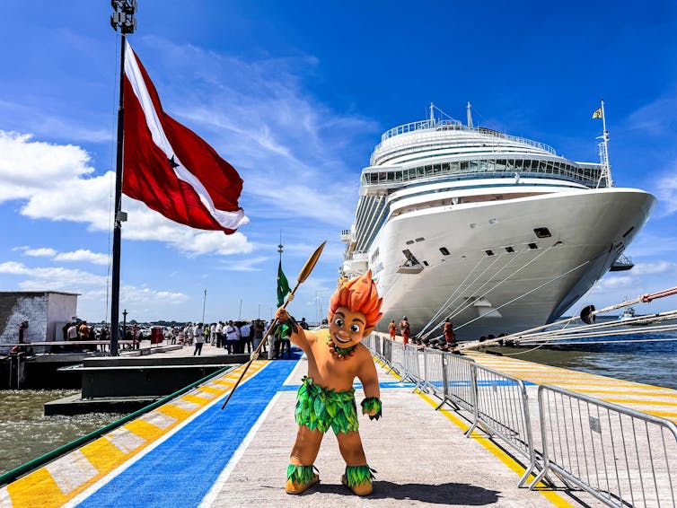 person dressed as a folklore figure at the Brazil climate talks with large ship in background.