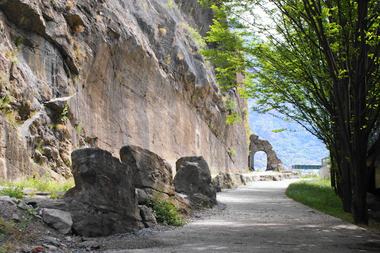 An old road next to an excavate cliff face with a stone arch in the distance.
