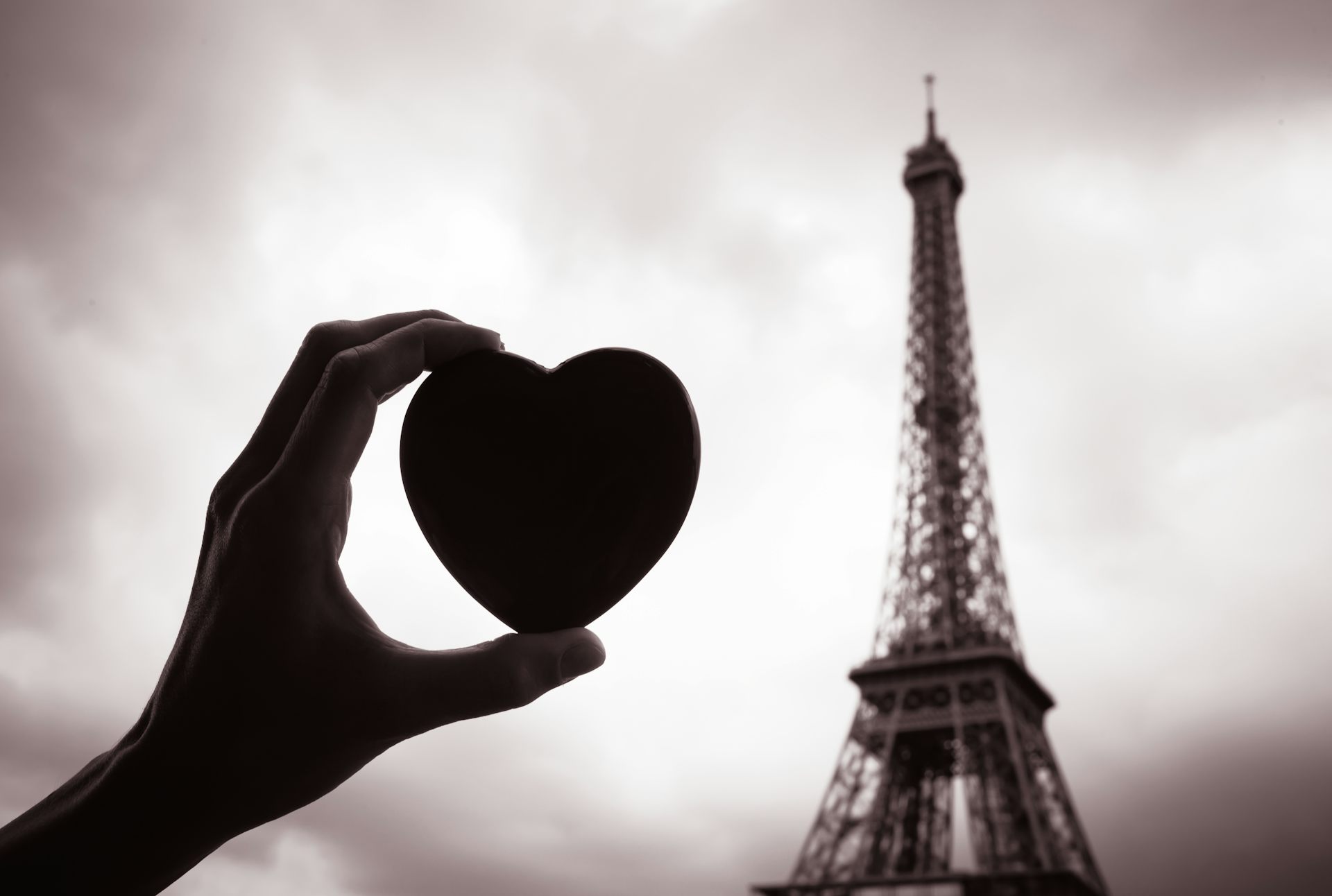 Une main tenant un coeur devant la Tour Eiffel.