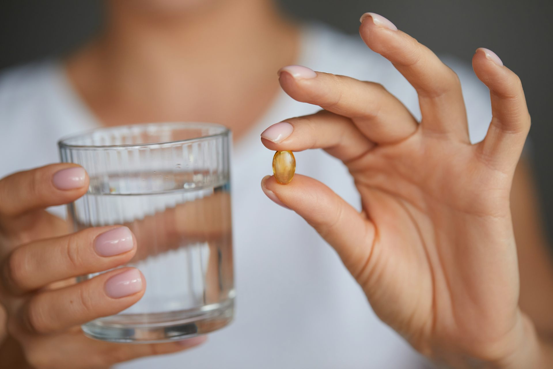 Una mujer muestra una pastilla anaranjada con una mano y sostiene un vaso con la otra.