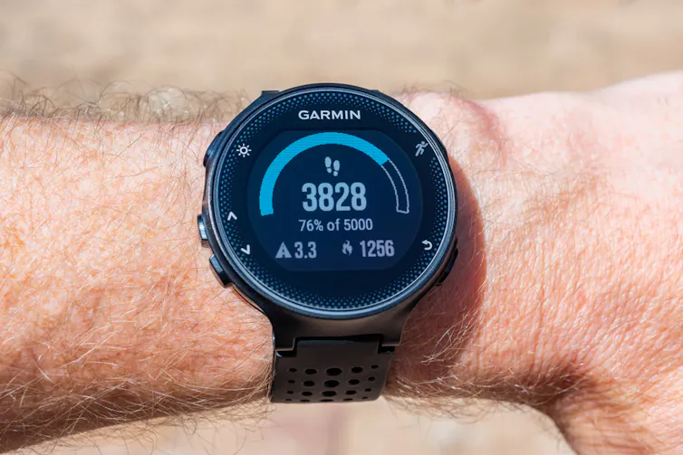 A digital tracker on a man's wrist showing step counts.