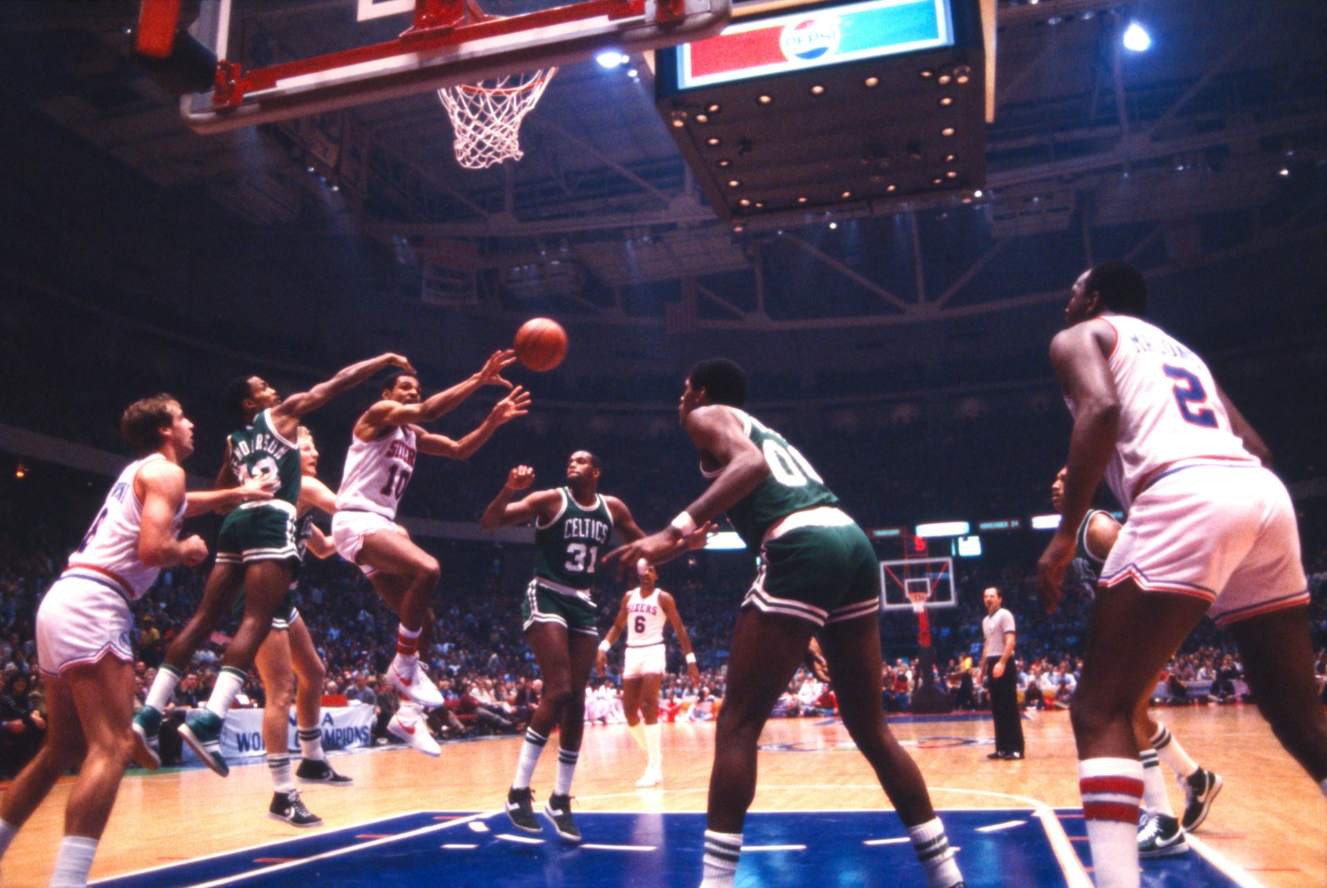 A player holding basketball jumps in air as opposing team tries to block a pass.