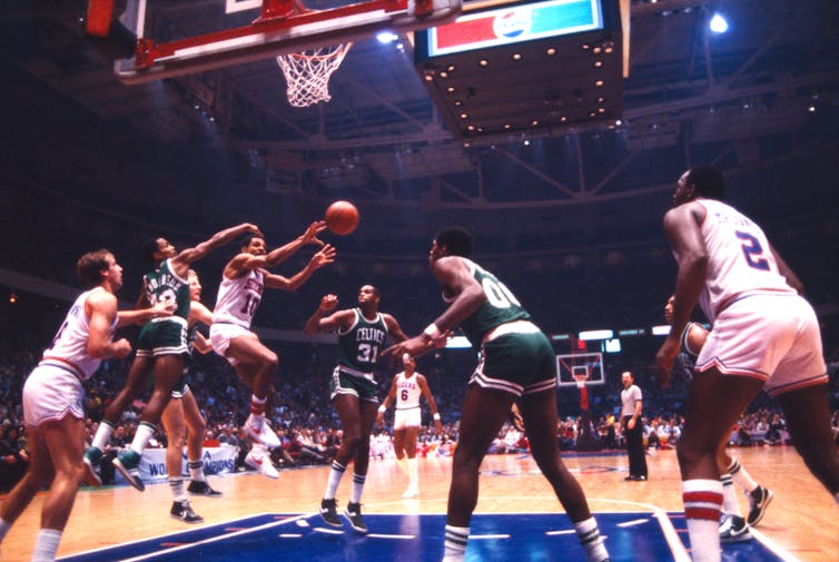 El jugador que sostiene la pelota salta en el aire mientras el equipo contrario intenta bloquear el pase.