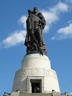 Una gran estatua de un hombre sosteniendo un bebé en una mano y una espada en la otra