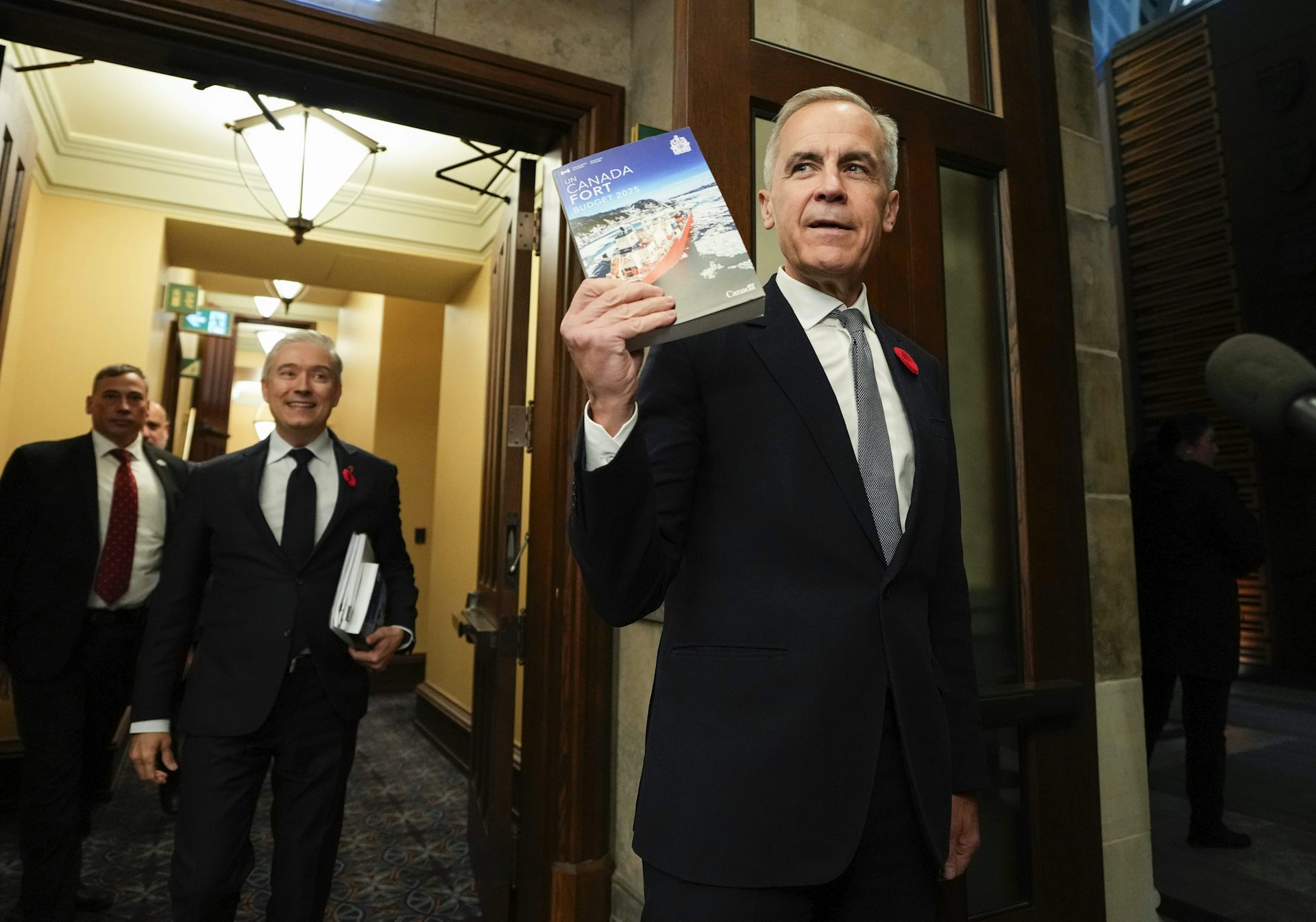 A man in suit and tie holding up a report that says 'Canada Fort.' 