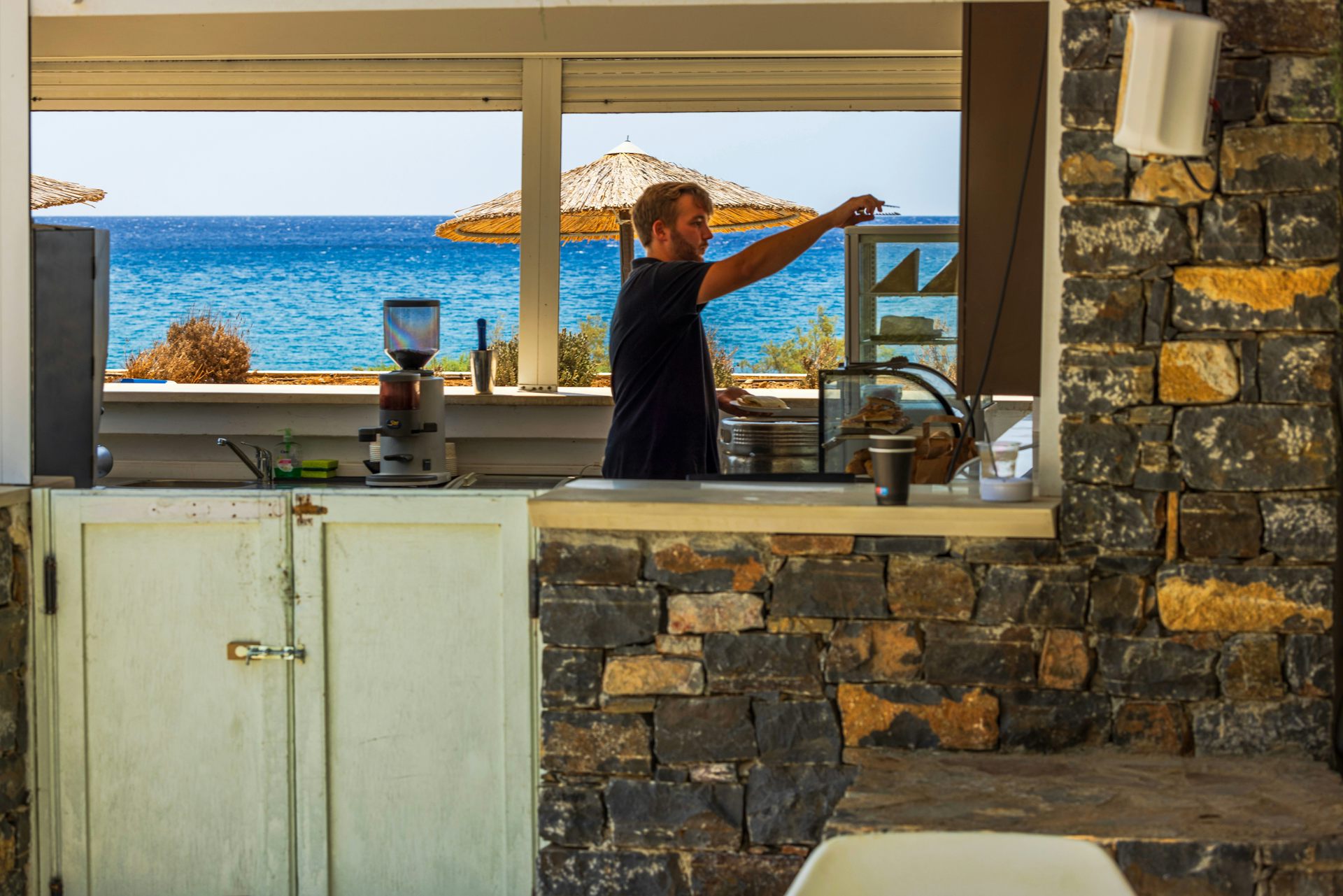 man working at a beachfront cafe in crete with the sea in the background