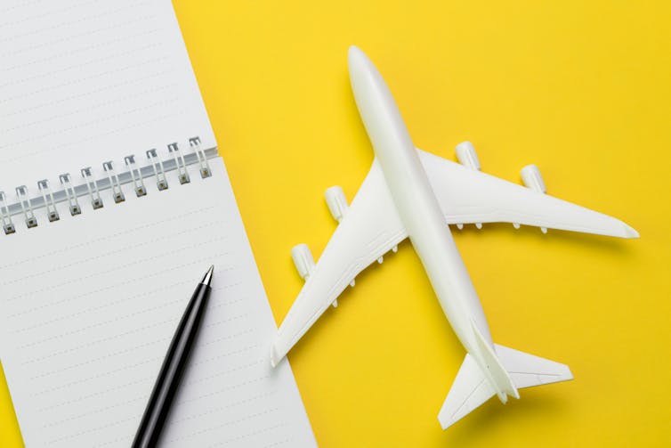 How a lot CO2 does your flight in reality produce? The way to know if carbon footprint claims are correct 1 yellow background, white toy plane and white notebook with pen