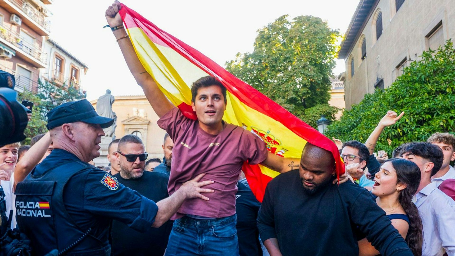 Un joven ondea una bandera rodeado policías y otras personas.