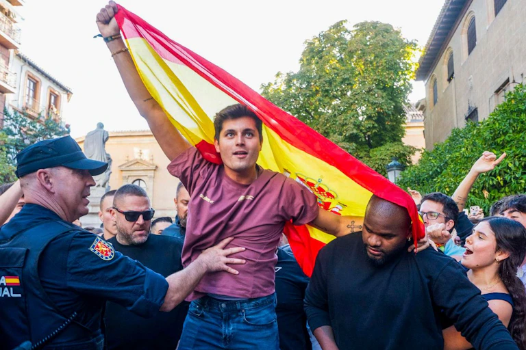 Un joven ondea una bandera rodeado policías y otras personas.