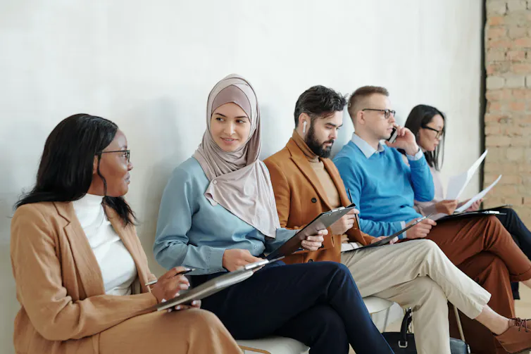 A row of people waiting on chairs to be interviewed for a job