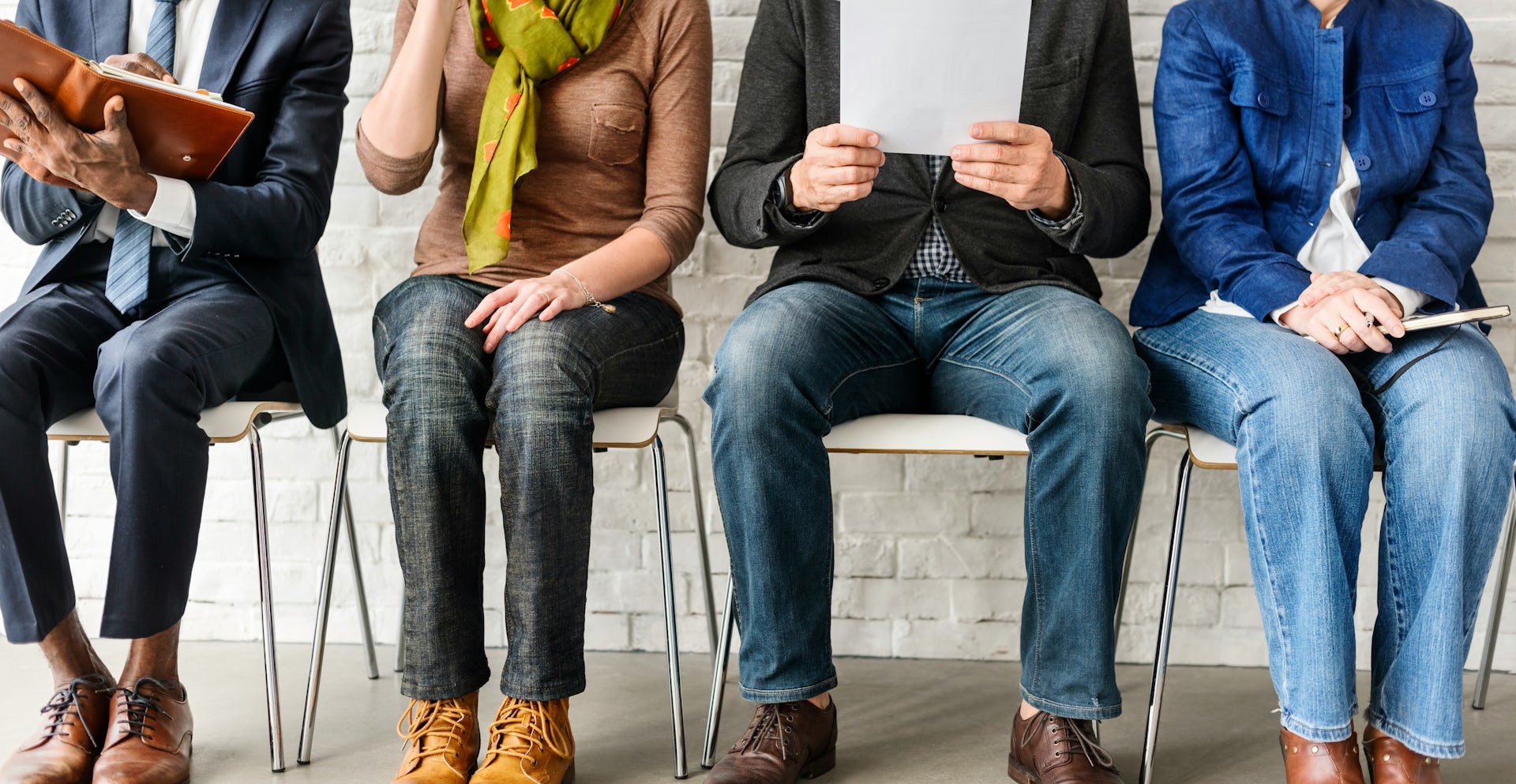 A row of people sitting in chairs, seen from the neck down