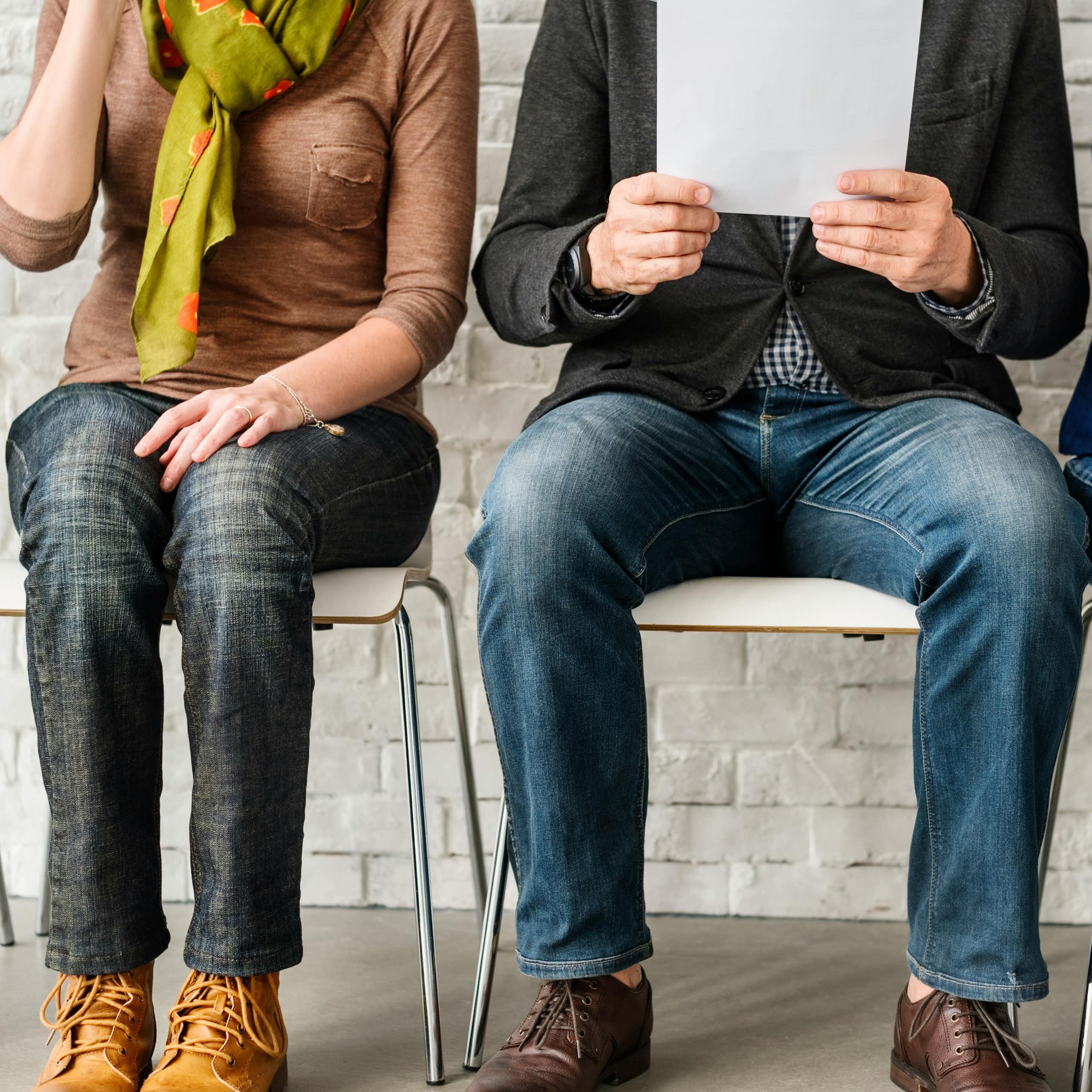 A row of people sitting in chairs, seen from the neck down