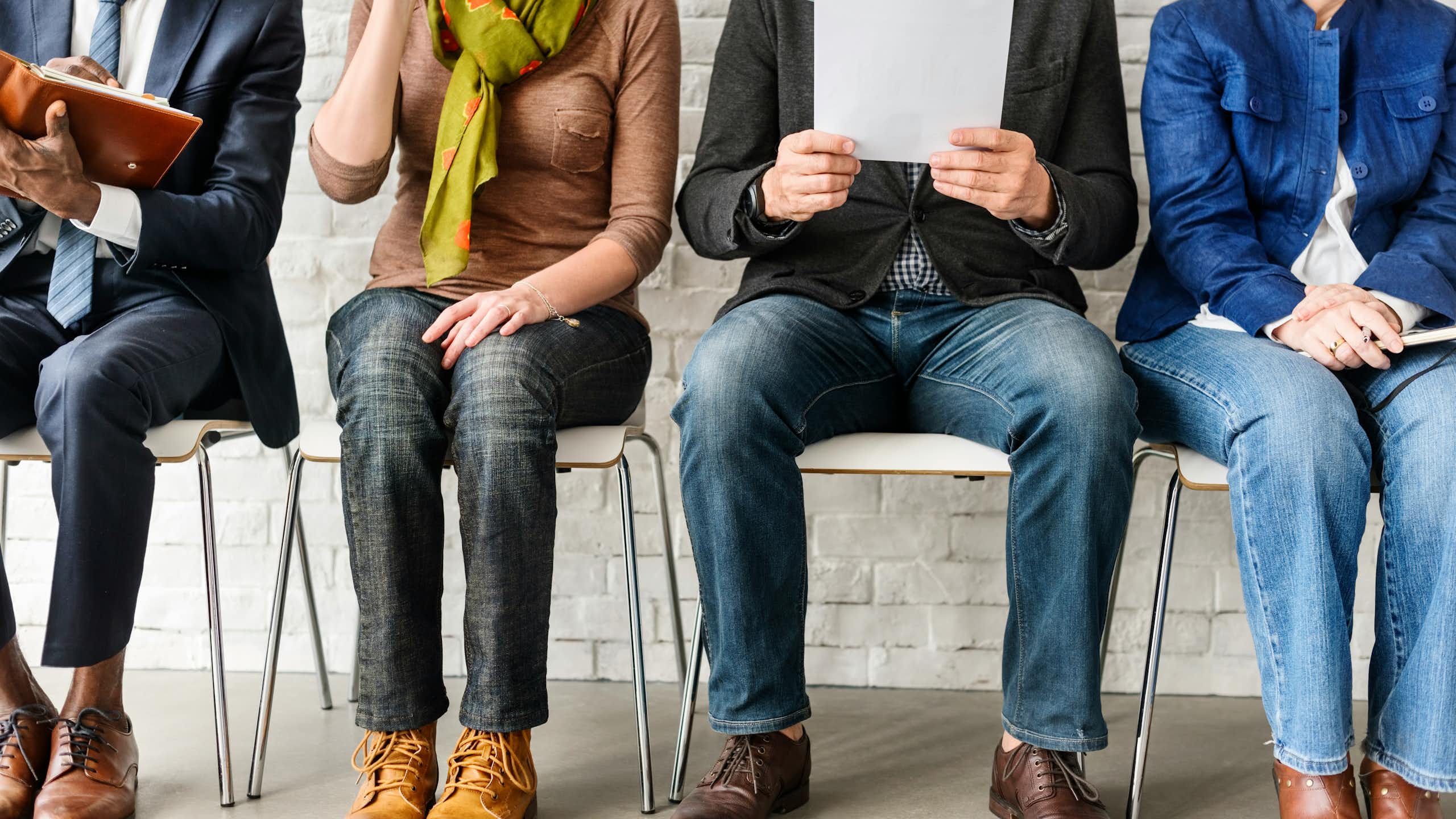 A row of people sitting in chairs, seen from the neck down