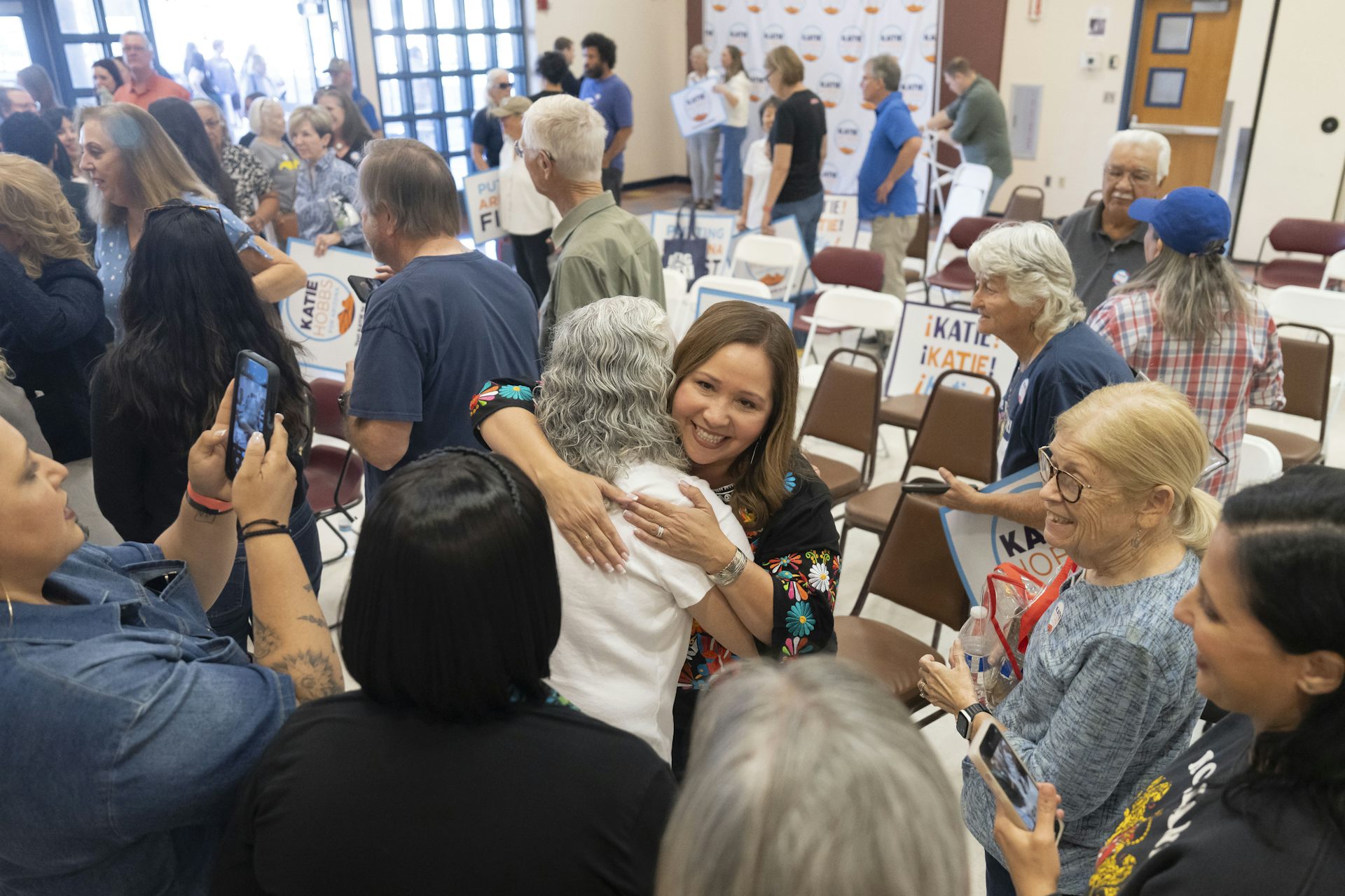 A woman hugs another woman in a room full of people.