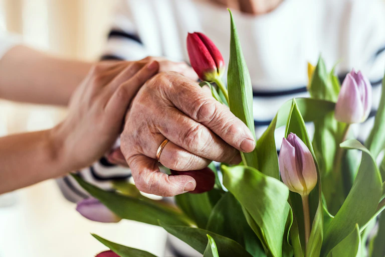 Close-up of an older woman's hand arranging tulips, with a younger woman's hands resting on her arm