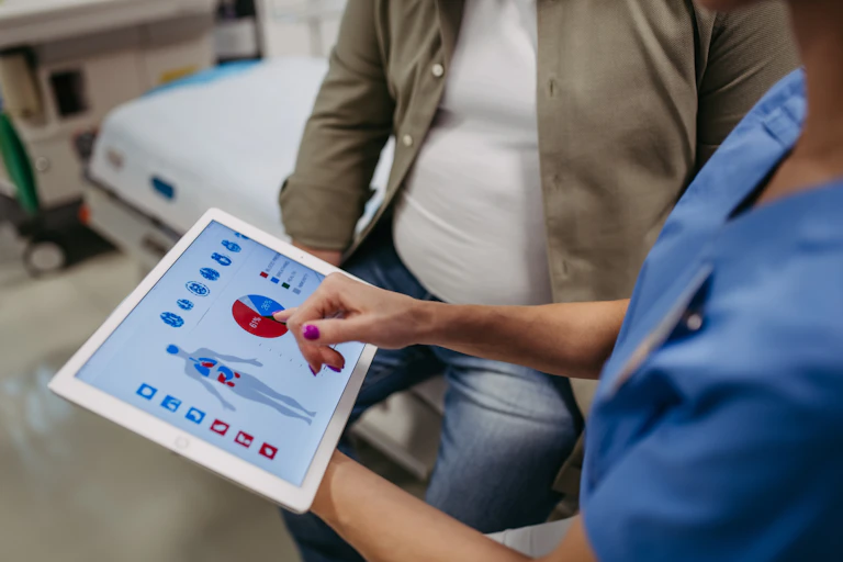 Un médico muestra en una tableta gráficos y la representación de un cuerpo humano a un paciente obeso.
