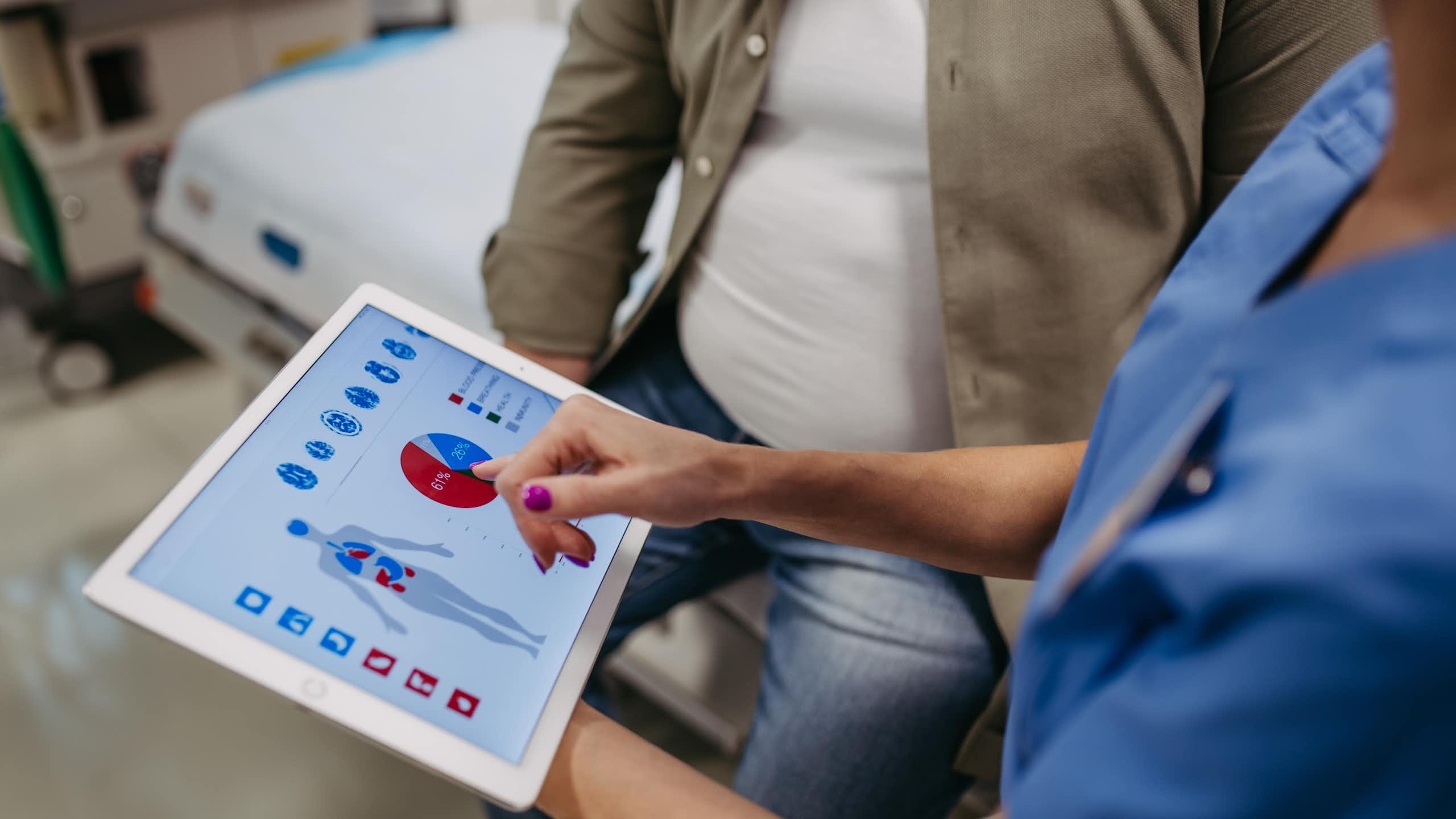 Un médico muestra en una tableta gráficos y la representación de un cuerpo humano a un paciente obeso.