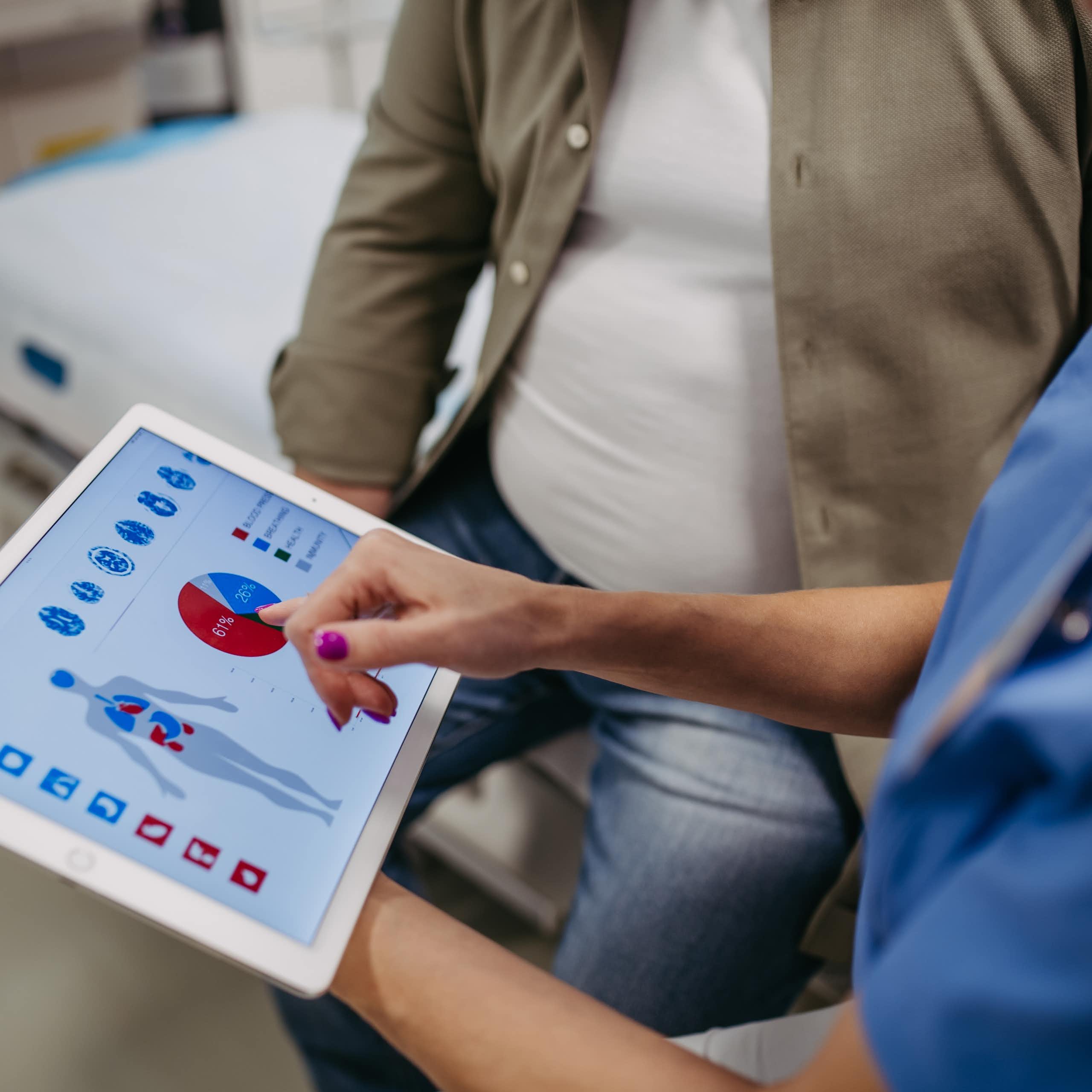 Un médico muestra en una tableta gráficos y la representación de un cuerpo humano a un paciente obeso.