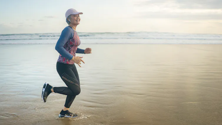 A middle-aged woman runs on a beach.