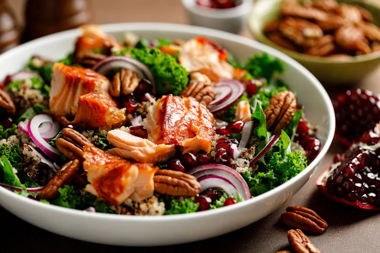 A salad in a white bowl, served with salmon, red onions, kale, pomegranate seeds and walnuts.