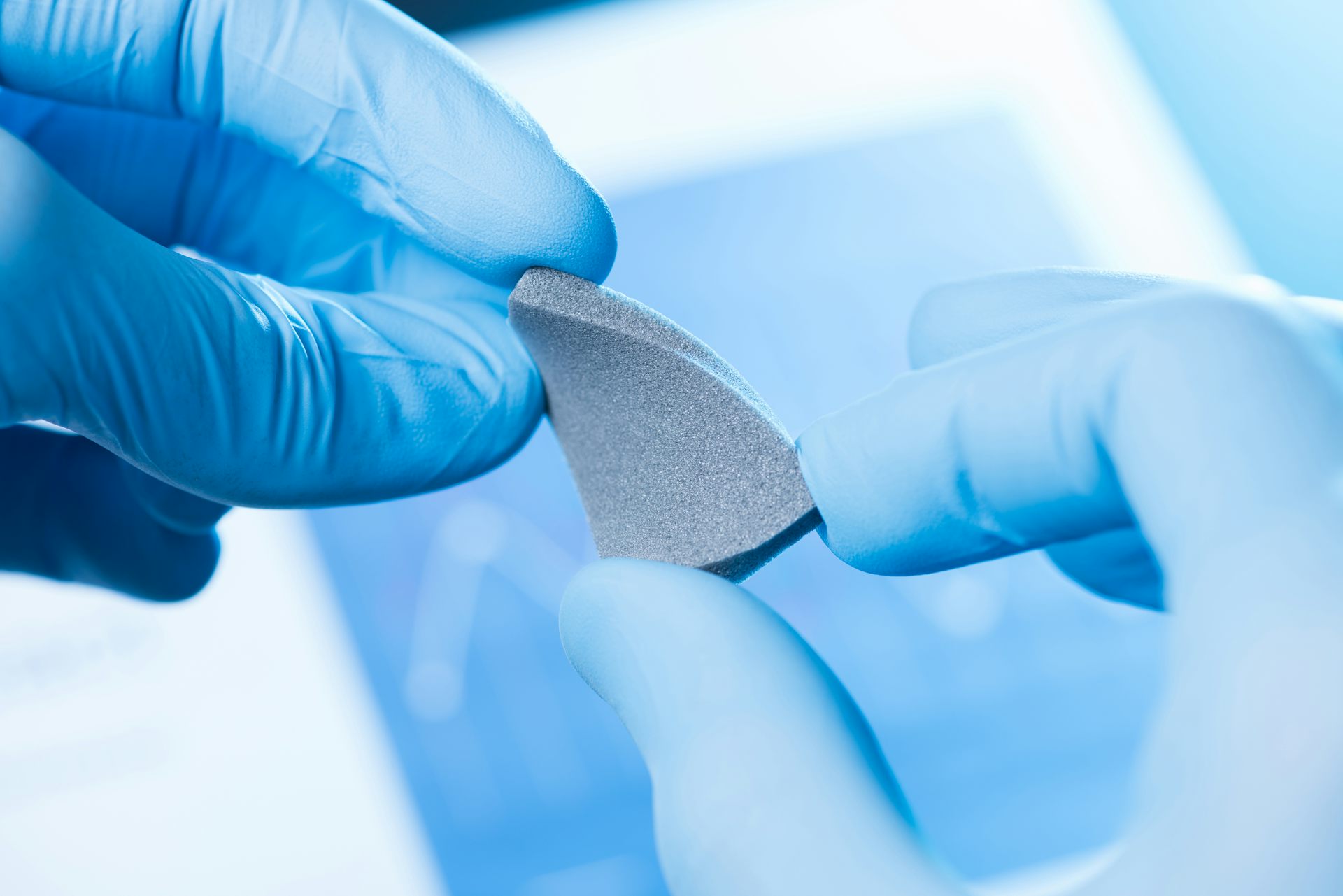 Unas manos enguantadas sostienen un pedazo de material gris.