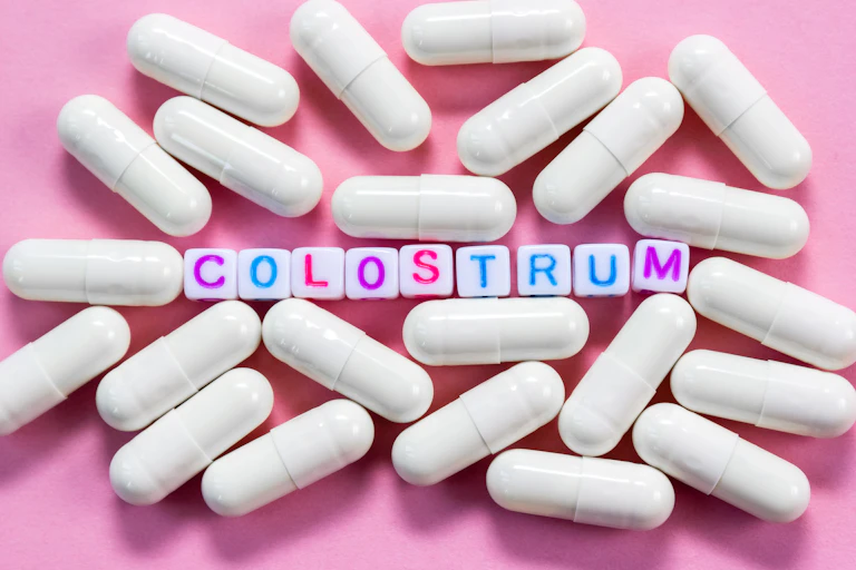 Word Colostrum. Plastic cubes with lettering surrounded by pharmaceutical pills on pink background close-up.