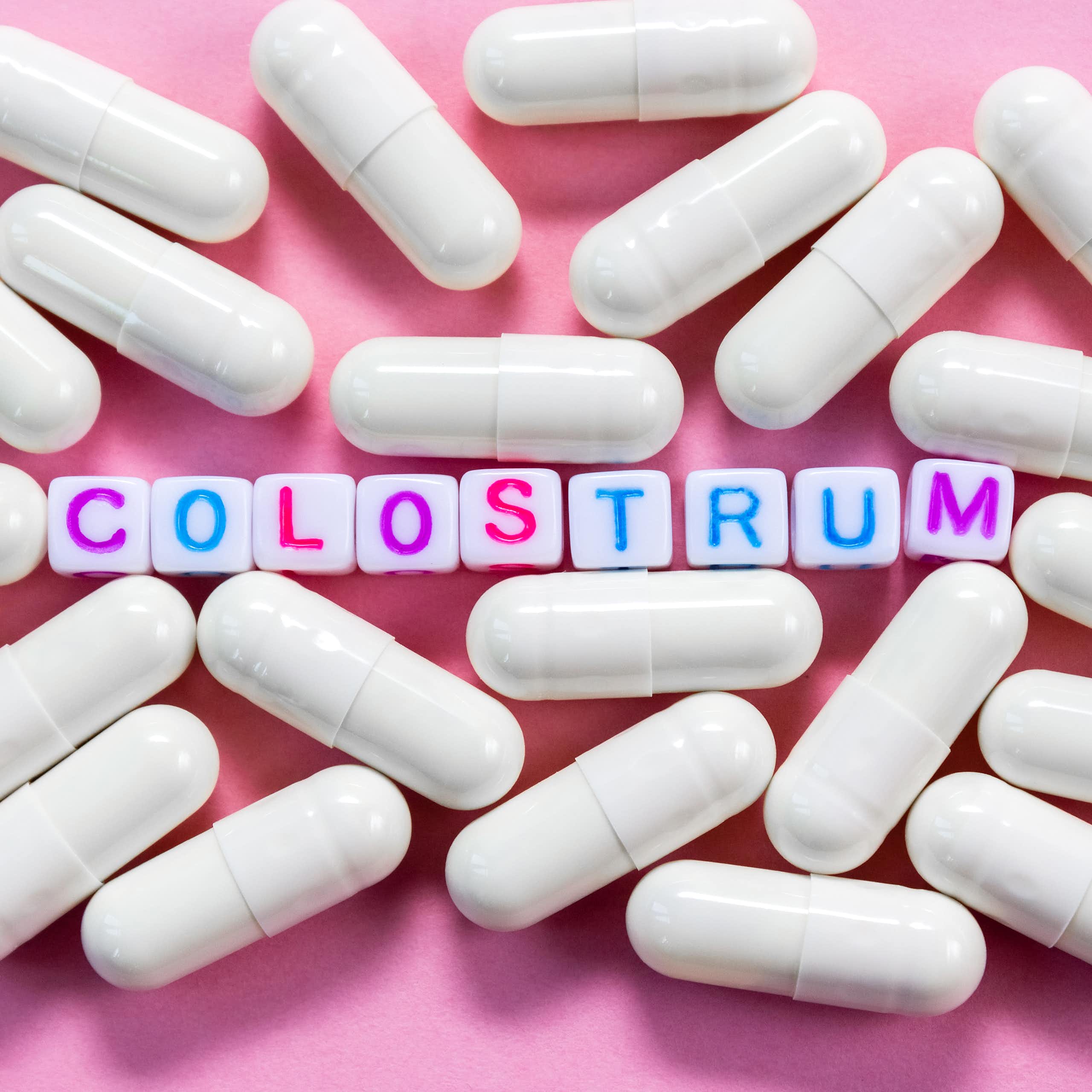 Word Colostrum. Plastic cubes with lettering surrounded by pharmaceutical pills on pink background close-up.