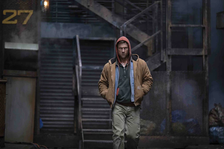 Glen Powell walking with his hood up