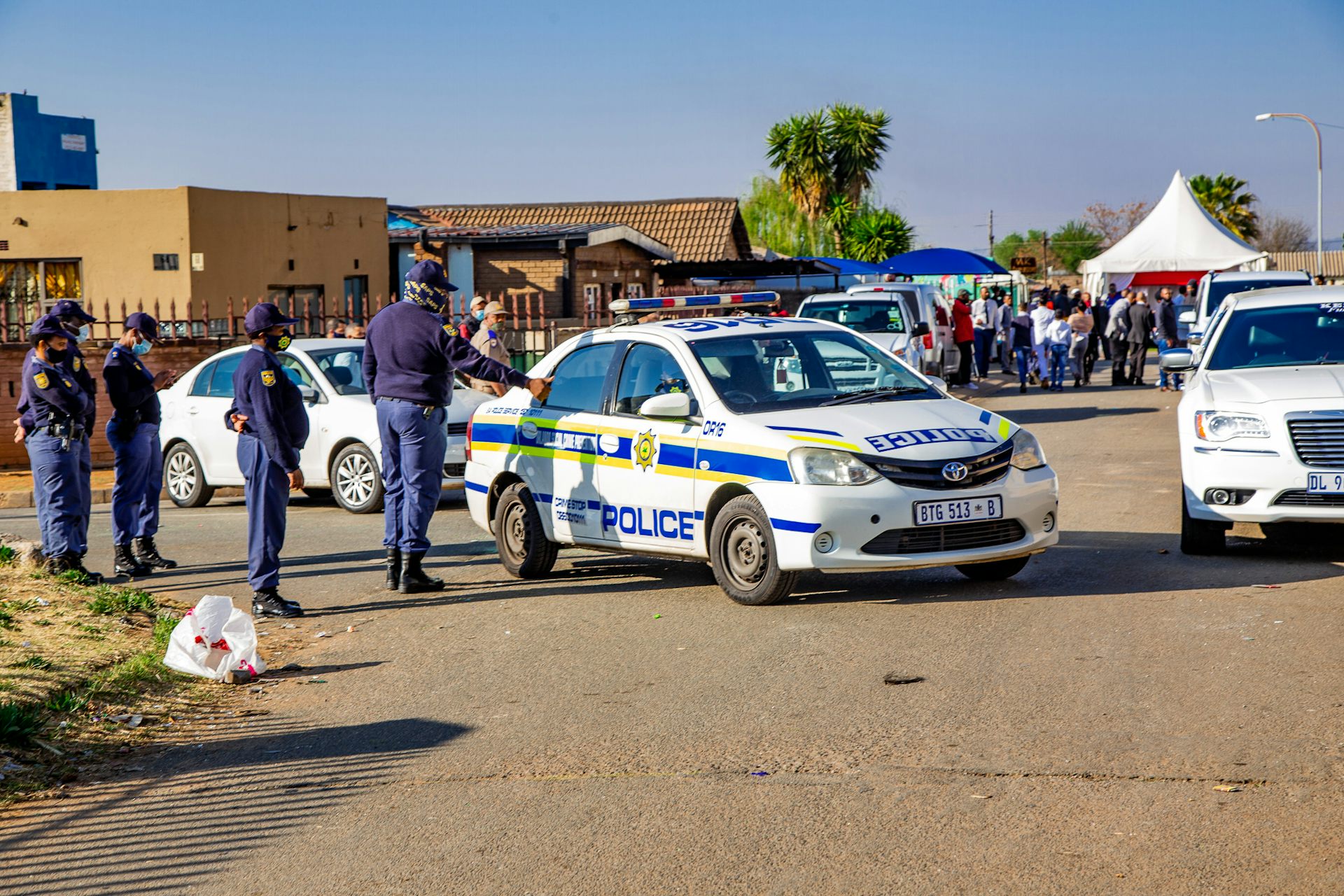 People in blue uniforms standing next to marked police vehicles